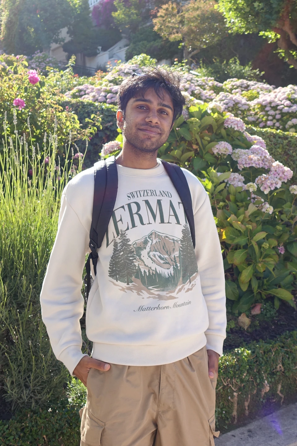 Adit smiling in front of flowering hydrangeas, wearing a cream Zermatt sweatshirt